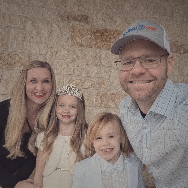 TJ, his wife, their daughter in a tiara and their son in a white suit, dressed up against a stone wall