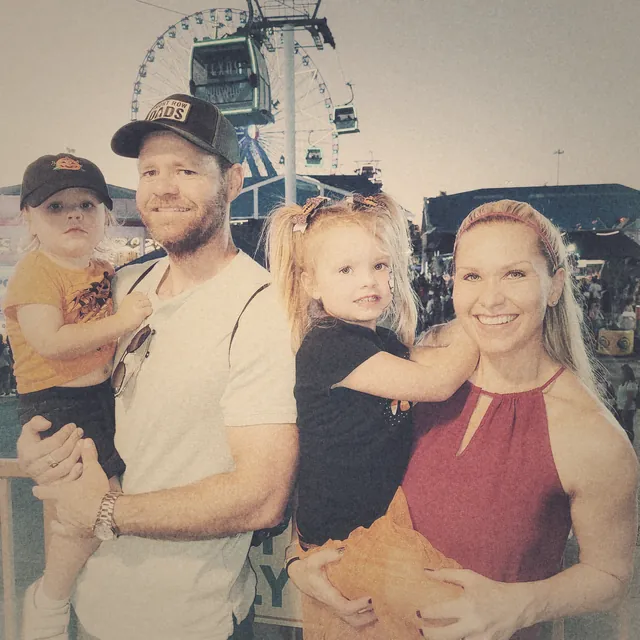 TJ with his wife and their two young kids, a Ferris wheel lit up behind them