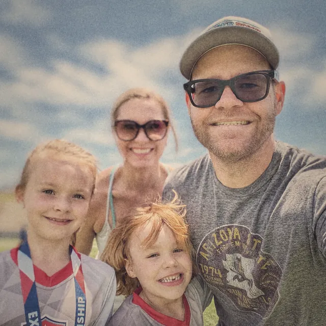 Selfie of TJ, his wife and their two kids on a sunny day, his daughter wearing a medal